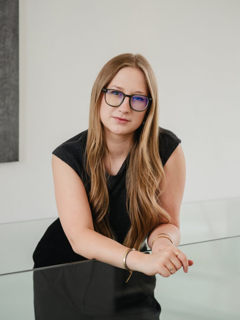 Amelie lächelnd an ihrem Schreibtisch