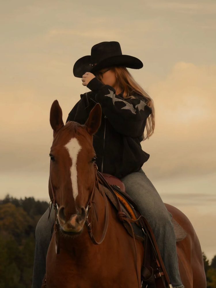 Amelie mit Cowboyhut auf einem Pferd im Abendlicht